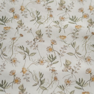 May include: A white fabric with a delicate floral pattern featuring small, light brown and yellow flowers and green leaves.