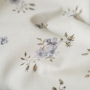 Könnte beinhalten: Weißer Stoff mit einem zarten Blumenmuster mit kleinen blauen Blüten und braunen Stielen.