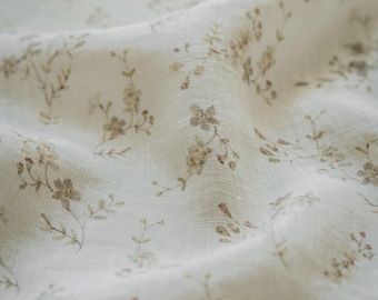 May include: A lightweight, off-white fabric featuring a delicate, repeating pattern of small, muted brown and soft pink wildflowers with thin green stems. The material has a visible, slightly textured weave and is draped in soft folds.