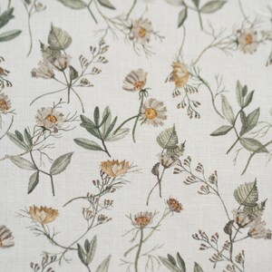 May include: A white fabric with a repeating pattern of small brown and yellow flowers and green leaves.