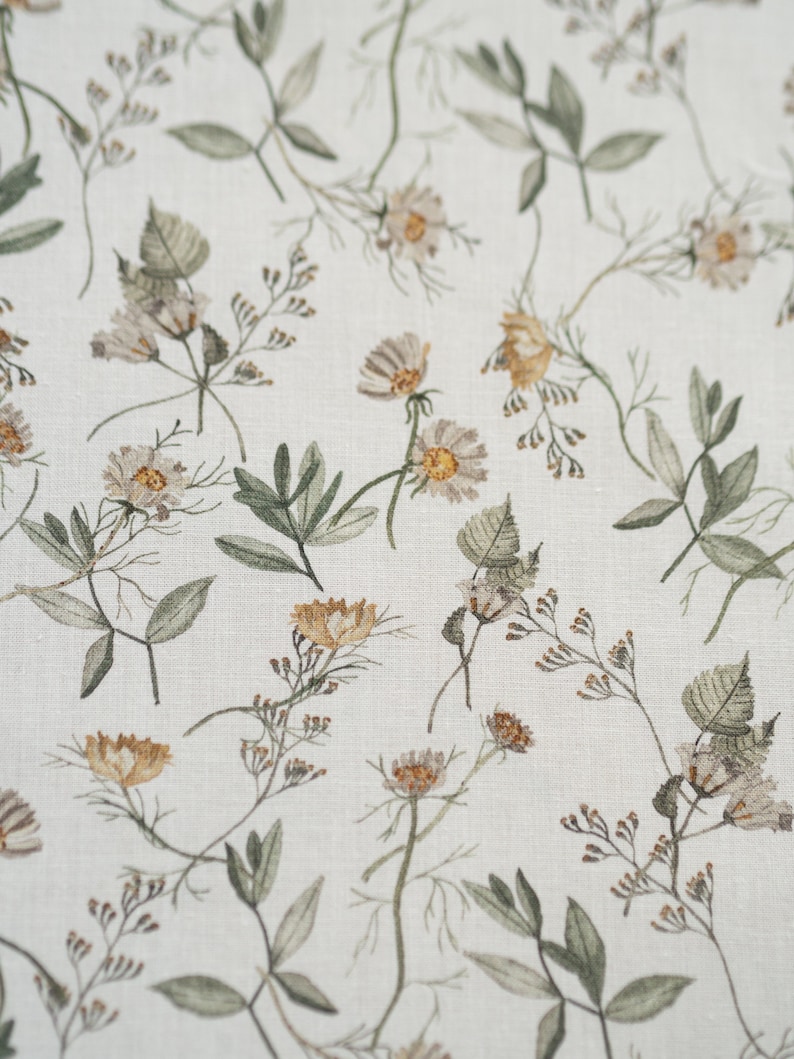 May include: A white fabric with a repeating pattern of small brown and yellow flowers and green leaves.