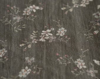 May include: A dark gray fabric featuring a repeating pattern of small, delicate white and light pink floral sprigs. The material has a visible woven texture with subtle vertical lines throughout, creating a soft and organic appearance.