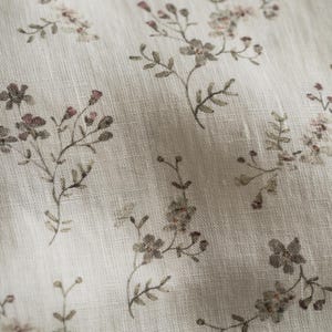 May include: A light beige fabric featuring a repeating pattern of small, delicate floral sprigs in muted shades of brown, green, and soft pink. The textile has a visible woven texture with subtle vertical lines throughout the material surface.