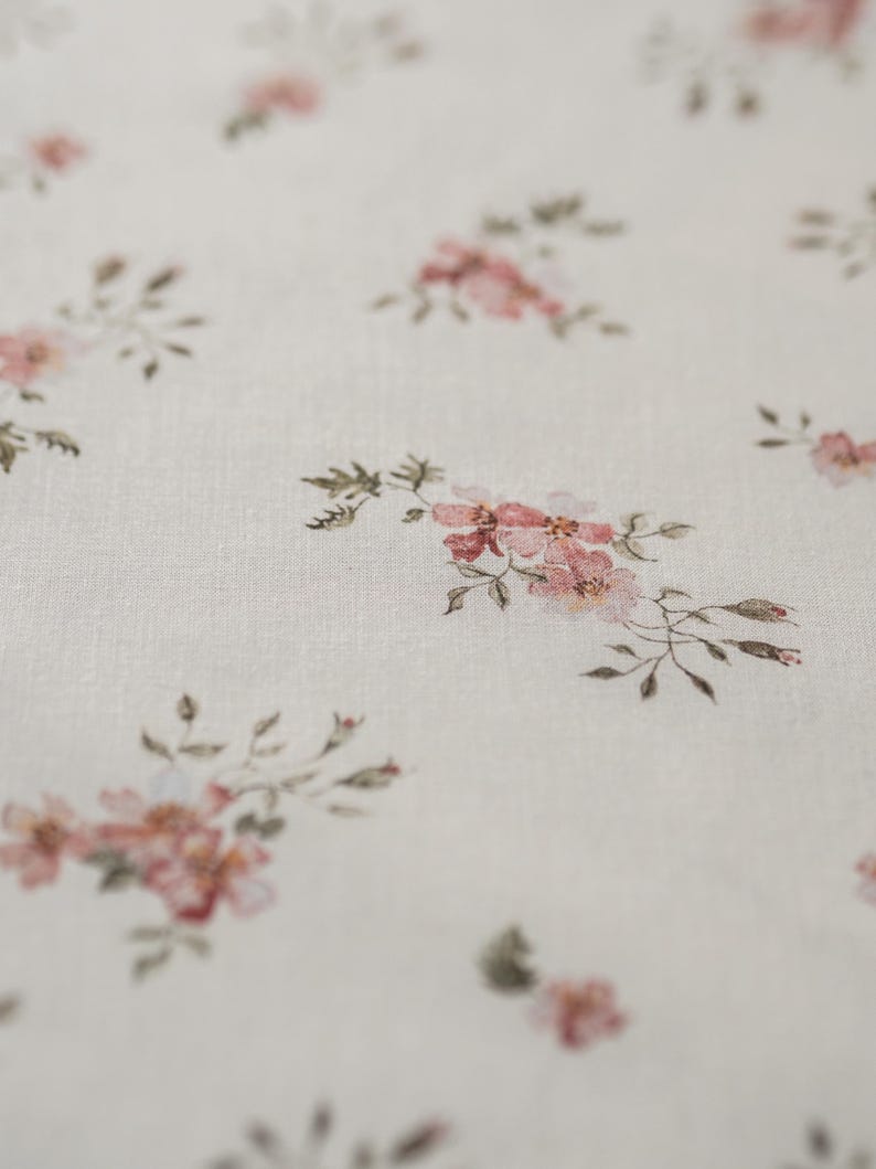 K&ouml;nnte beinhalten: Ein wei&szlig;er Stoff mit einem zarten Blumenmuster mit kleinen rosa Bl&uuml;ten und gr&uuml;nen Bl&auml;ttern.