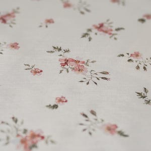 K&ouml;nnte beinhalten: Wei&szlig;er Stoff mit einem zarten Blumenmuster mit kleinen rosa Bl&uuml;ten und gr&uuml;nen Bl&auml;ttern.