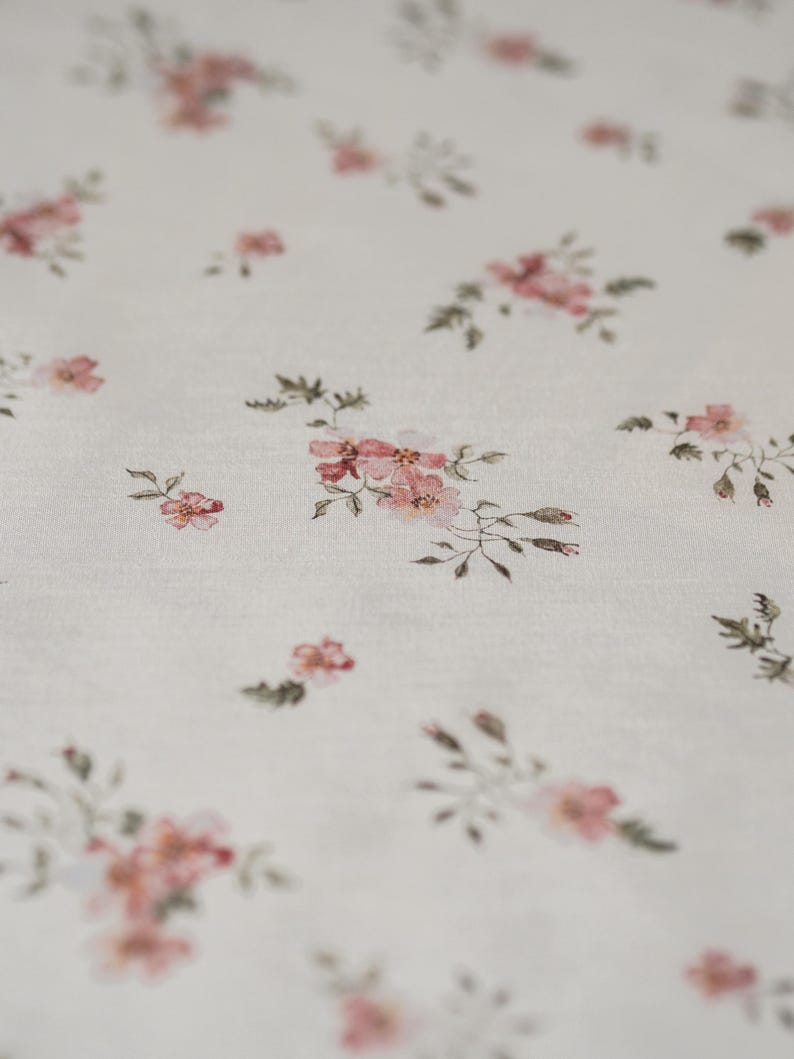 K&ouml;nnte beinhalten: Wei&szlig;er Stoff mit einem zarten Blumenmuster mit kleinen rosa Bl&uuml;ten und gr&uuml;nen Bl&auml;ttern.