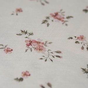 K&ouml;nnte beinhalten: Wei&szlig;er Stoff mit einem zarten Blumenmuster mit kleinen rosa Bl&uuml;ten und gr&uuml;nen Bl&auml;ttern.