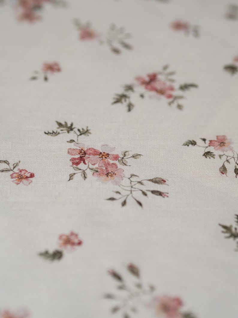 K&ouml;nnte beinhalten: Wei&szlig;er Stoff mit einem zarten Blumenmuster mit kleinen rosa Bl&uuml;ten und gr&uuml;nen Bl&auml;ttern.