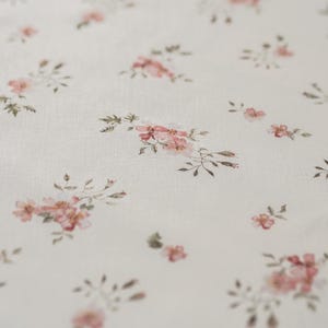 K&ouml;nnte beinhalten: Wei&szlig;er Stoff mit einem zarten Blumenmuster mit kleinen rosa Bl&uuml;ten und gr&uuml;nen Bl&auml;ttern.