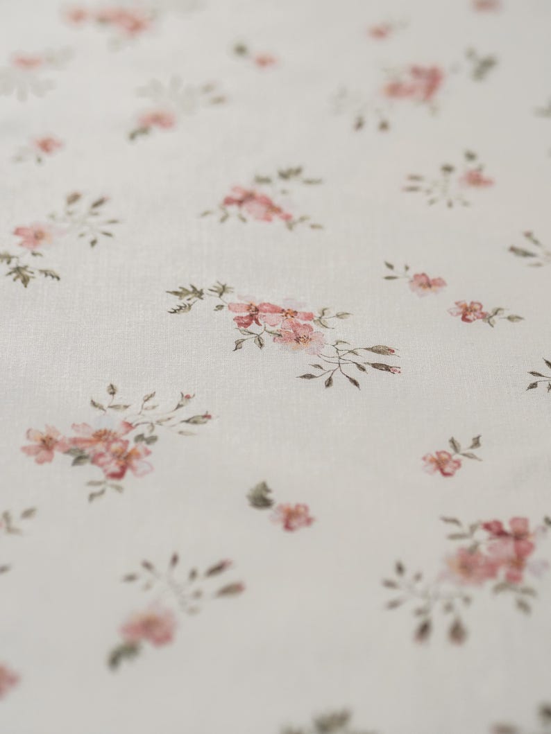 K&ouml;nnte beinhalten: Wei&szlig;er Stoff mit einem zarten Blumenmuster mit kleinen rosa Bl&uuml;ten und gr&uuml;nen Bl&auml;ttern.