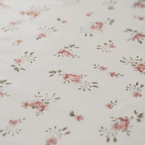 K&ouml;nnte beinhalten: Ein wei&szlig;er Stoff mit einem zarten Blumenmuster. Die Blumen sind rosa und gr&uuml;n und sind zuf&auml;llig &uuml;ber den Stoff verteilt.