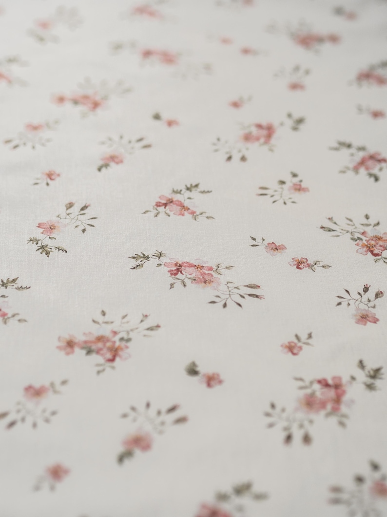 K&ouml;nnte beinhalten: Ein wei&szlig;er Stoff mit einem zarten Blumenmuster. Die Blumen sind rosa und gr&uuml;n und sind zuf&auml;llig &uuml;ber den Stoff verteilt.