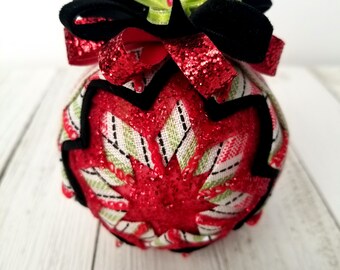 May include: A red, green, and black Christmas ornament with a glittery finish. The ornament is made of fabric and has a starburst design.
