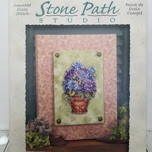 May include: A cross stitch kit featuring a hydrangea basket. The kit includes the fabric, floss, and a mounting frame. The kit is from Stone Path Studio.