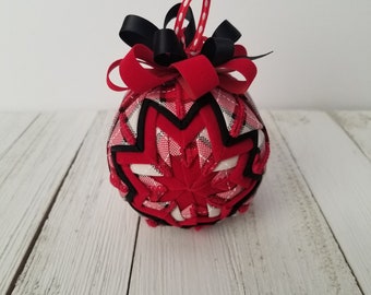 May include: Red and black plaid Christmas ornament with a black bow. The ornament is made of fabric and has a white polka dot ribbon for hanging.