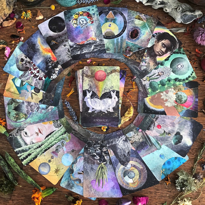 K&ouml;nnte beinhalten: Eine kreisf&ouml;rmige Auslage von Tarotkarten mit Aquarell-Illustrationen. Die Karten zeigen eine Vielzahl von Bildern, darunter Tiere, Naturszenen und Himmelsk&ouml;rper. Die Karten sind in einem Kreis um eine zentrale Karte angeordnet, auf der "ANOMALY" steht.