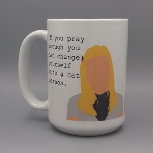 Puede incluir: Taza de cer&aacute;mica blanca con un asa grande. La taza presenta un gr&aacute;fico de una mujer con cabello rubio y el texto: "Si rezas lo suficiente, puedes convertirte en una persona de gatos."
