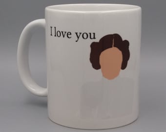Może przedstawiać: Biały ceramiczny kubek z uchwytem. Kubek zawiera napis "I love you" oraz rysunkową ilustrację twarzy kobiety z brązowymi włosami i opaloną twarzą. Kubek jest przedmiotem z motywem Gwiezdnych Wojen.