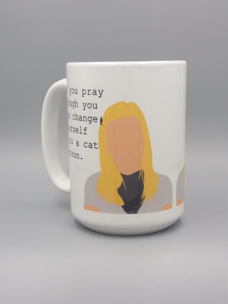 Puede incluir: Taza de cer&aacute;mica blanca con asa, con una ilustraci&oacute;n de una mujer rubia y el texto: "Si rezas lo suficiente, puedes convertirte en una persona de gatos."