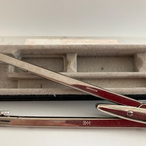 May include: A silver compass with a black case. The compass has a knob on the top and the words "GERMANY" and "K+E" printed on it.