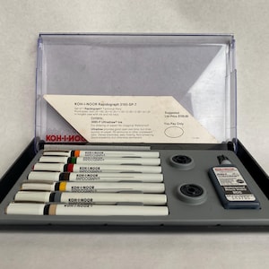 May include: A set of KOH-I-NOOR Rapidograph technical pens in a clear plastic case. The set includes several white pens with colored bands, ink, and accessories. The case is open, revealing the contents, with text on the packaging.