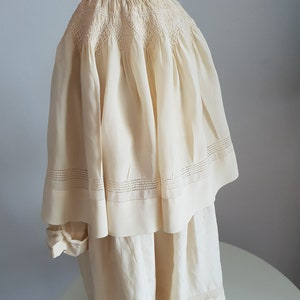 May include: A white cotton dress with a smocked bodice and a tiered skirt. The dress has delicate lace trim around the neckline and hem.