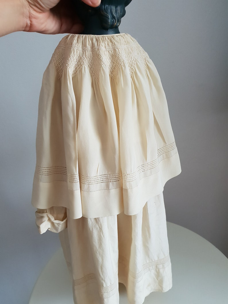 May include: A white cotton dress with a smocked bodice and a tiered skirt. The dress has delicate lace trim around the neckline and hem.