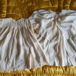 May include: Two vintage white cotton baby dresses with smocking and lace details. The dresses are laid out on a yellow quilted fabric.