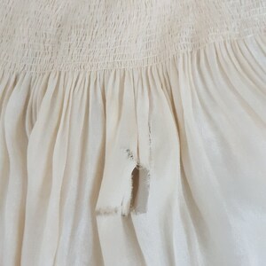 May include: A close-up of a white fabric with a gathered ruffle and a small tear in the fabric.