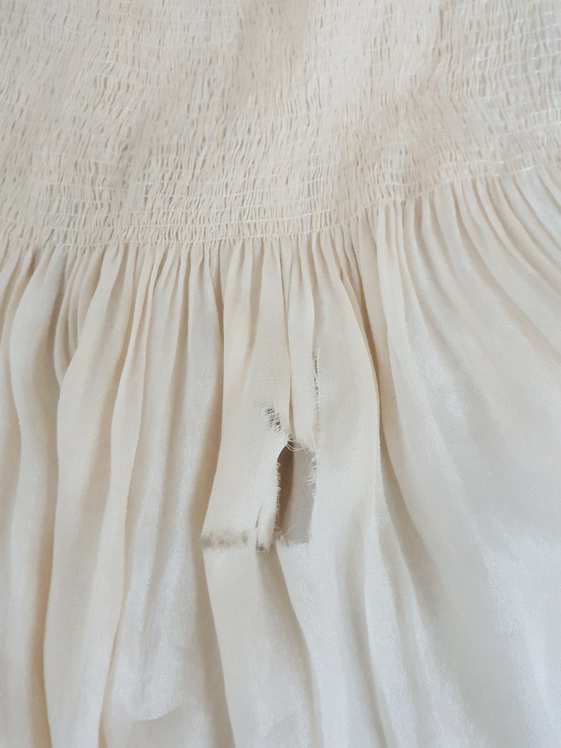 May include: A close-up of a white fabric with a gathered ruffle and a small tear in the fabric.