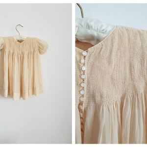 May include: A pale yellow vintage baby dress with a smocked bodice and pearl buttons. The dress has short puffed sleeves and a gathered skirt.