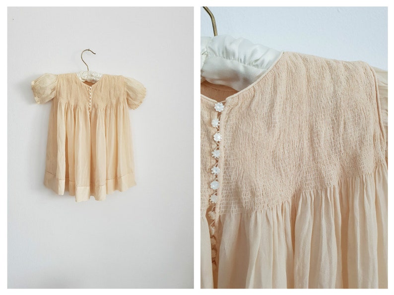May include: A pale yellow vintage baby dress with a smocked bodice and pearl buttons. The dress has short puffed sleeves and a gathered skirt.