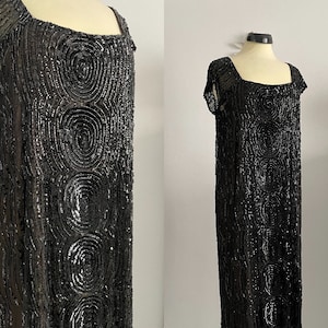 May include: A black beaded dress with a circular pattern. The dress has short sleeves and a scoop neck.