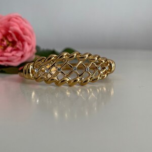 May include: A gold-toned bracelet with a woven design and clear rhinestones.