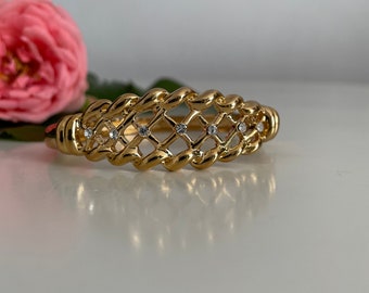 Puede incluir: Un brazalete dorado con un diseño tejido y brillantes transparentes.
