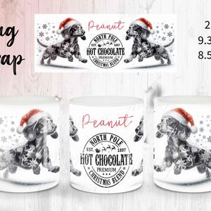 May include: White ceramic mug featuring a black and white dachshund wearing a Santa hat, with snowflakes and the text "Peanut North Pole Hot Chocolate Premium Christmas Blend".