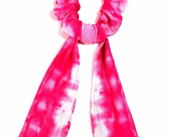 May include: A pink and white tie-dye scrunchie with long tails. The scrunchie is made of soft fabric and has a tie-dye pattern.
