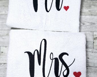 Peut inclure: Deux serviettes de bain rectangulaires blanches avec du texte brodé en noir et de petits cœurs rouges. La serviette du haut affiche le texte "Mr." avec un cœur rouge, tandis que celle du bas affiche "Mrs." avec un cœur rouge en écriture cursive.