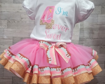 May include: A white short-sleeved shirt with a pink ice cream cone shaped number 4 and the text I'm four-ever sweet, paired with a pink tulle tutu skirt featuring a ribbon trim with a brown waffle cone pattern and light blue icing design.