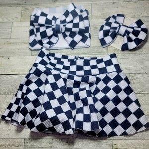 May include: A three-piece set featuring a black and white checkered pattern. The set includes a skirt, a headband with a large bow, and a smaller bow. The skirt is a flared style, and the headband and bow are made of the same checkered fabric.