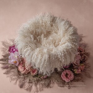 May include: A white fluffy newborn photography prop with a brown and beige fringe and pink flowers around the edge.