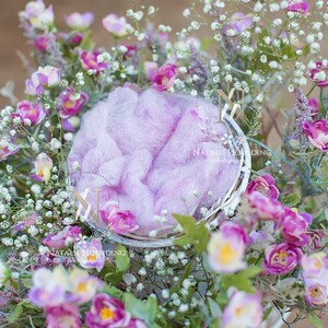 Puede incluir: Una cesta de mimbre blanca llena de un material esponjoso de color rosa similar a una nube, rodeada de un ramo de flores rosas y blancas.