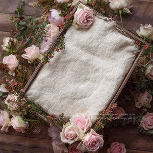 May include: A white fabric backdrop in a wooden frame surrounded by pink roses and greenery. The backdrop is ideal for newborn photography.
