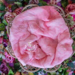 May include: A pink, fluffy, cotton-like newborn photography prop in a woven basket. The prop is surrounded by a variety of colorful flowers.