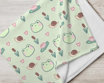 Può includere: Una coperta verde e bianca con un motivo ripetitivo di rane, lumache, cuori e ninfee.