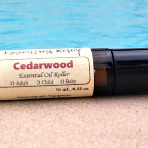 May include: A brown glass roller bottle with a white label that reads "Cedarwood Essential Oil Roller" with the text "O Adult O Child O Baby" and "10 mL / 0.33 oz."