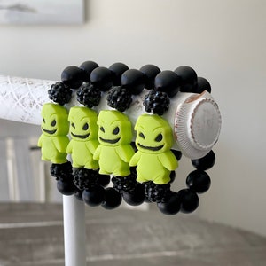 May include: Four black bead bracelets with green character charms. Each charm is a green character with a black face and a wide smile. The charms are attached to the bracelets with black beads.