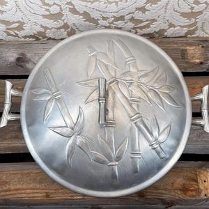 May include: A silver metal serving dish with two handles. The dish has an embossed design of bamboo stalks and leaves.