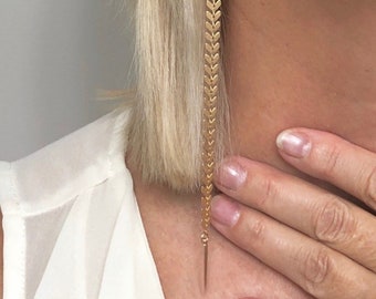 May include: Gold long chain earrings with a chevron pattern. The earrings are very long and dangle down to the neck.