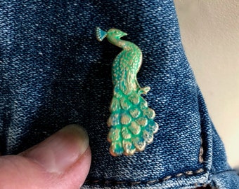 May include: A green and gold peacock pin on a blue denim jacket.